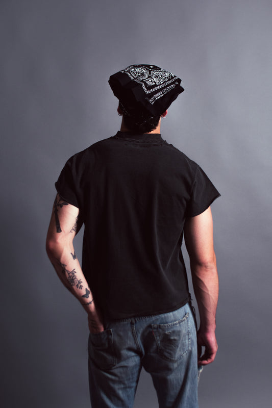 Person wearing a black t-shirt and beanie with tattoos on arms against a gray background