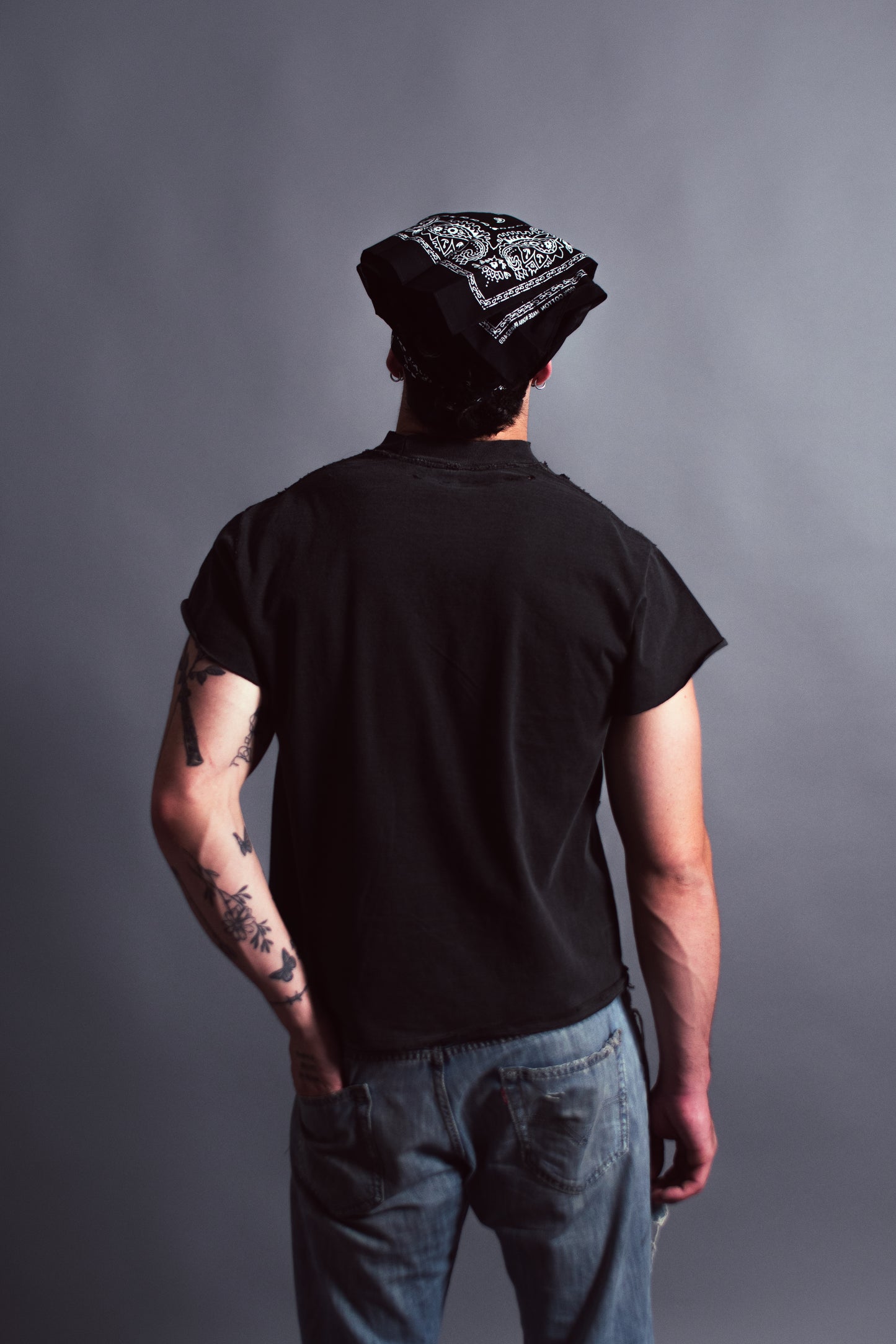 Person wearing a black t-shirt and beanie with tattoos on arms against a gray background
