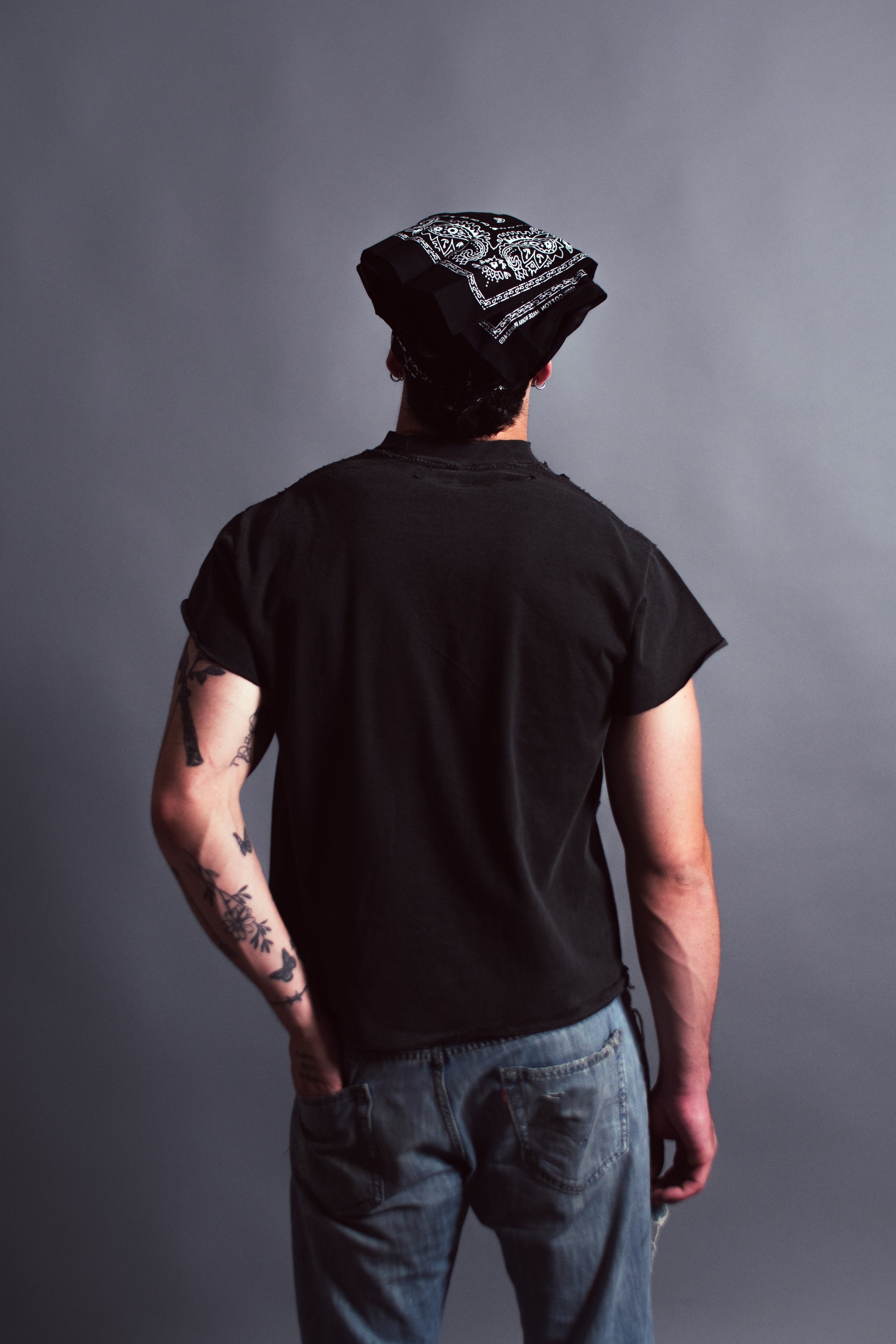 Person wearing a black t-shirt and beanie with tattoos on arms against a gray background